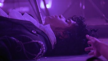 Movie still from “Purple Rain” (1984), directed by Albert Magnoli – A woman laying on the ground in a purple room; Medium shot, Overhead angle