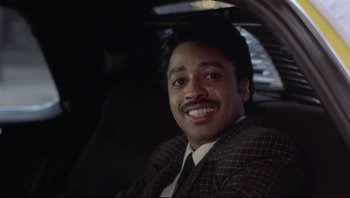 Movie still from “Purple Rain” (1984), directed by Albert Magnoli – A man sitting in the back seat of a car smiling; Close Up shot, Low angle