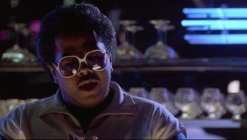 Movie still from “Purple Rain” (1984), directed by Albert Magnoli – A man with glasses is sitting at a bar; Close Up shot, Low angle