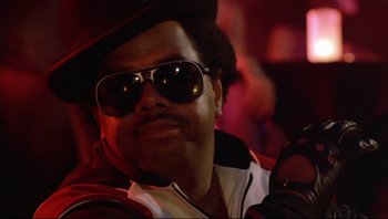 Movie still from “Purple Rain” (1984), directed by Albert Magnoli – A man wearing sunglasses and a hat is smiling; Close Up shot, Low angle