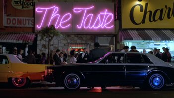 Movie still from “Purple Rain” (1984), directed by Albert Magnoli – A car parked on the side of the road in front of a restaurant; Extreme Wide shot, Low angle