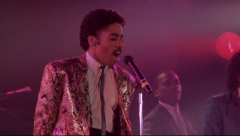 Movie still from “Purple Rain” (1984), directed by Albert Magnoli – A man is singing into a microphone on stage; Medium shot, Low angle