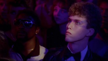 Movie still from “Purple Rain” (1984), directed by Albert Magnoli – A group of young people sitting in front of a crowd; Close Up shot, Over the shoulder angle