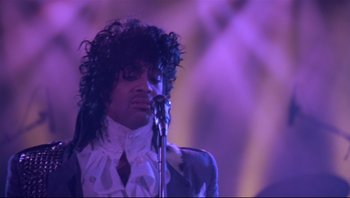 Movie still from “Purple Rain” (1984), directed by Albert Magnoli – A person holding a microphone on a stage; Close Up shot, Low angle