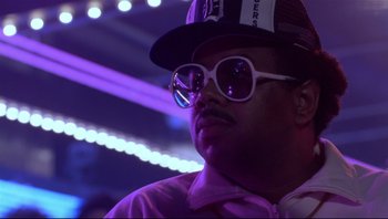 Movie still from “Purple Rain” (1984), directed by Albert Magnoli – A man wearing a hat and sunglasses in front of purple lights; Close Up shot, Low angle
