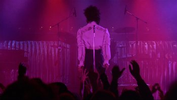 Movie still from “Purple Rain” (1984), directed by Albert Magnoli – A man standing on a stage in front of a crowd; Wide shot, Low angle