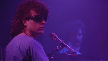 Movie still from “Purple Rain” (1984), directed by Albert Magnoli – A man with sunglasses and a microphone in front of a microphone stand; Close Up shot, Over the shoulder angle