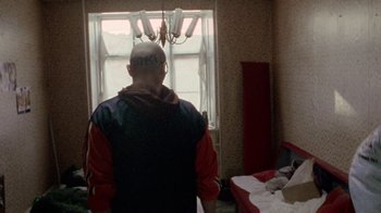 Movie still from “Pusher” (1996), directed by Nicolas Winding Refn – A man standing in front of a window in a room; Wide shot, Over the shoulder angle
