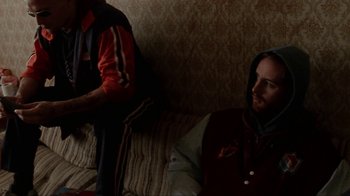 Movie still from “Pusher” (1996), directed by Nicolas Winding Refn – A man sitting on a couch next to another man; Medium shot, Over the shoulder angle
