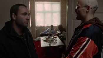 Movie still from “Pusher” (1996), directed by Nicolas Winding Refn – A group of men sitting at a table in front of a window; Medium shot, Over the shoulder angle
