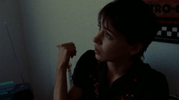 Movie still from “Pusher” (1996), directed by Nicolas Winding Refn – A young woman holding her hand up to her face; Close Up shot, High angle