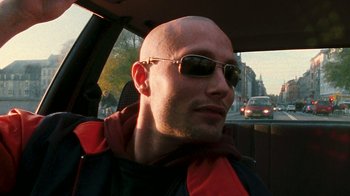 Movie still from “Pusher” (1996), directed by Nicolas Winding Refn – A bald man wearing sunglasses in the back of a car; Close Up shot, Low angle