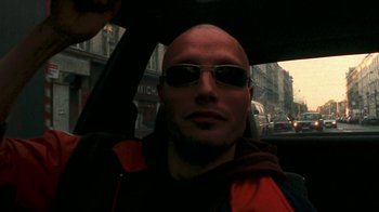 Movie still from “Pusher” (1996), directed by Nicolas Winding Refn – A man with sunglasses is sitting in the back of a car; Close Up shot, Low angle