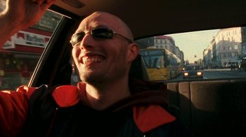 Movie still from “Pusher” (1996), directed by Nicolas Winding Refn – A bald man with sunglasses is sitting in the driver's seat of a car; Close Up shot, Low angle