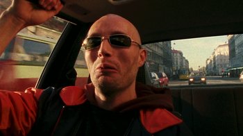 Movie still from “Pusher” (1996), directed by Nicolas Winding Refn – A bald man wearing sunglasses sitting in the back of a car; Close Up shot, Low angle