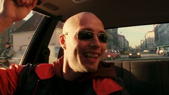 Movie still from “Pusher” (1996), directed by Nicolas Winding Refn – A bald man wearing sunglasses in the back of a car; Close Up shot, Low angle