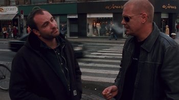 Movie still from “Pusher” (1996), directed by Nicolas Winding Refn – Two men standing on the side of the street talking; Medium shot, Low angle