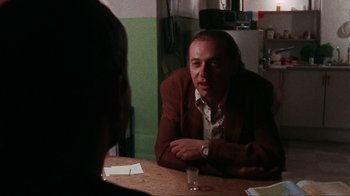 Movie still from “Pusher” (1996), directed by Nicolas Winding Refn – A man sitting at a table with a glass of water in front of him; Close Up shot, Over the shoulder angle