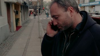 Movie still from “Pusher” (1996), directed by Nicolas Winding Refn – A man on a cell phone on the sidewalk; Close Up shot, Low angle