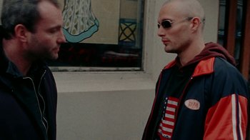 Movie still from “Pusher” (1996), directed by Nicolas Winding Refn – Two men standing next to each other in front of a building; Close Up shot, Over the shoulder angle