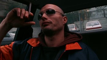Movie still from “Pusher” (1996), directed by Nicolas Winding Refn – A bald man with sunglasses is taking a selfie; Close Up shot, Low angle
