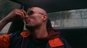Movie still from “Pusher” (1996), directed by Nicolas Winding Refn – A bald man with sunglasses in the back of a car; Close Up shot, Low angle