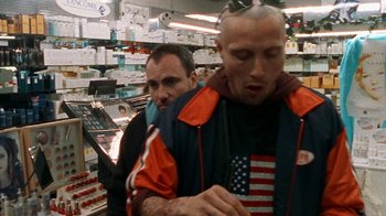 Movie still from “Pusher” (1996), directed by Nicolas Winding Refn – A man with an american flag tattoo on his head and a man with an american flag tattoo on his face; Medium shot, Over the shoulder angle