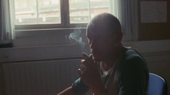 Movie still from “Pusher” (1996), directed by Nicolas Winding Refn – A man sitting in front of a window smoking a cigarette; Close Up shot, Over the shoulder angle