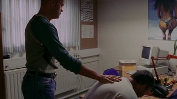 Movie still from “Pusher” (1996), directed by Nicolas Winding Refn – A man standing next to a person in a room; Medium shot, Over the shoulder angle