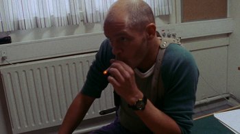 Movie still from “Pusher” (1996), directed by Nicolas Winding Refn – A man sitting in front of an electric device; Medium shot, Low angle