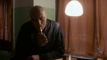 Movie still from “Pusher” (1996), directed by Nicolas Winding Refn – A bald man lighting a cigarette in a room; Close Up shot, Low angle