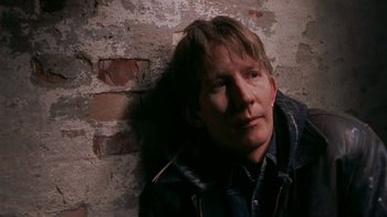 Movie still from “Pusher” (1996), directed by Nicolas Winding Refn – A man leaning against a brick wall with his head turned to the side; Close Up shot, High angle