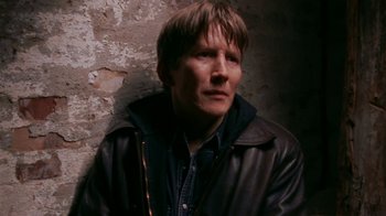Movie still from “Pusher” (1996), directed by Nicolas Winding Refn – A man wearing a leather jacket standing in front of a wall; Close Up shot, High angle