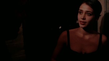 Movie still from “Pusher” (1996), directed by Nicolas Winding Refn – A woman in a black top is smiling for the camera; Close Up shot, Over the shoulder angle