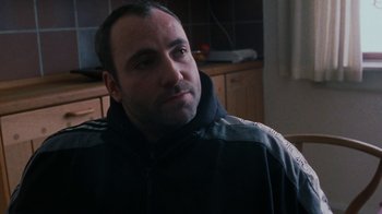 Movie still from “Pusher” (1996), directed by Nicolas Winding Refn – A person sitting in a room; Close Up shot, Over the shoulder angle