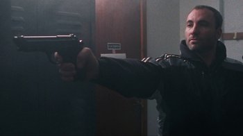 Movie still from “Pusher” (1996), directed by Nicolas Winding Refn – A man holding a gun in a room; Medium shot, Low angle