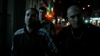 Movie still from “Pusher” (1996), directed by Nicolas Winding Refn – A group of men standing next to each other on a street; Medium shot, Low angle