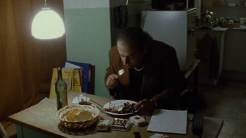 Movie still from “Pusher” (1996), directed by Nicolas Winding Refn – A man sitting at a dinner table eating food; Medium shot, High angle