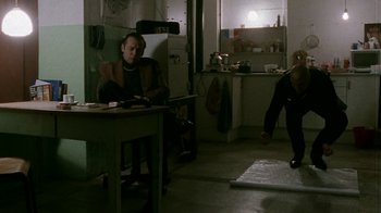 Movie still from “Pusher” (1996), directed by Nicolas Winding Refn – A man sitting at a table in a kitchen; Wide shot, Low angle