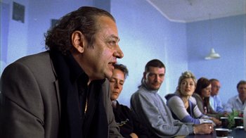 Movie still from “Pusher III” (2005), directed by Nicolas Winding Refn – A group of men and women sitting in a room; Close Up shot, Over the shoulder angle