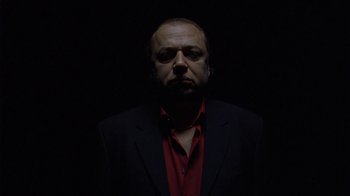 Movie still from “Pusher III” (2005), directed by Nicolas Winding Refn – A man wearing a suit and red shirt in the dark; Close Up shot, Low angle