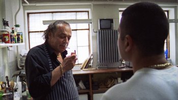 Movie still from “Pusher III” (2005), directed by Nicolas Winding Refn – A man smoking a cigarette in front of another man in a room; Medium shot, Over the shoulder angle