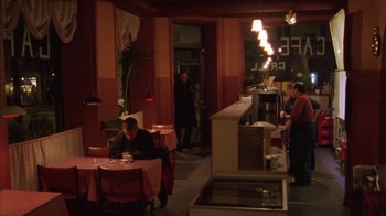 Movie still from “Pusher III” (2005), directed by Nicolas Winding Refn – A man sitting at a table in front of two other people; Wide shot, High angle