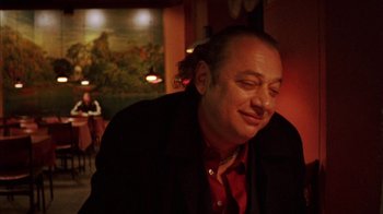 Movie still from “Pusher III” (2005), directed by Nicolas Winding Refn – A man sitting in front of a painting in a room; Close Up shot, Low angle