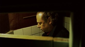 Movie still from “Pusher III” (2005), directed by Nicolas Winding Refn – A man in a suit is looking into a bathroom stall; Close Up shot, Low angle