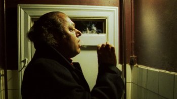 Movie still from “Pusher III” (2005), directed by Nicolas Winding Refn – A man smoking a cigarette in front of an open window; Close Up shot, Low angle