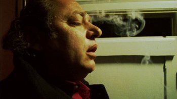 Movie still from “Pusher III” (2005), directed by Nicolas Winding Refn – A man in a red shirt is smoking a cigarette; Close Up shot, Low angle