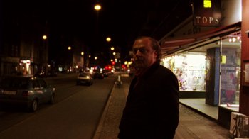 Movie still from “Pusher III” (2005), directed by Nicolas Winding Refn – A man standing on the side of the street at night; Medium shot, Low angle