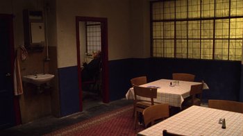 Movie still from “Pusher III” (2005), directed by Nicolas Winding Refn – A man sitting at a table in front of a window; Wide shot, High angle