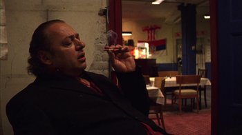 Movie still from “Pusher III” (2005), directed by Nicolas Winding Refn – A man sitting in a room smoking a cigarette; Medium shot, Low angle